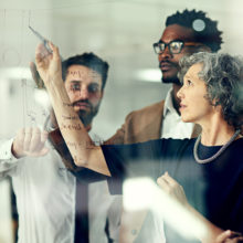 Cropped shot of a group of businesspeople brainstorming with notes on a glass wall in an office