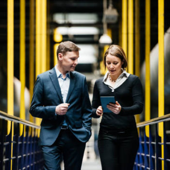 Two Business Person Walking A Dark Factory Hallway and talking about their latest projects