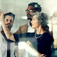 Cropped shot of a group of businesspeople brainstorming with notes on a glass wall in an office