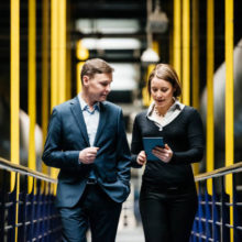 Two Business Person Walking A Dark Factory Hallway and talking about their latest projects